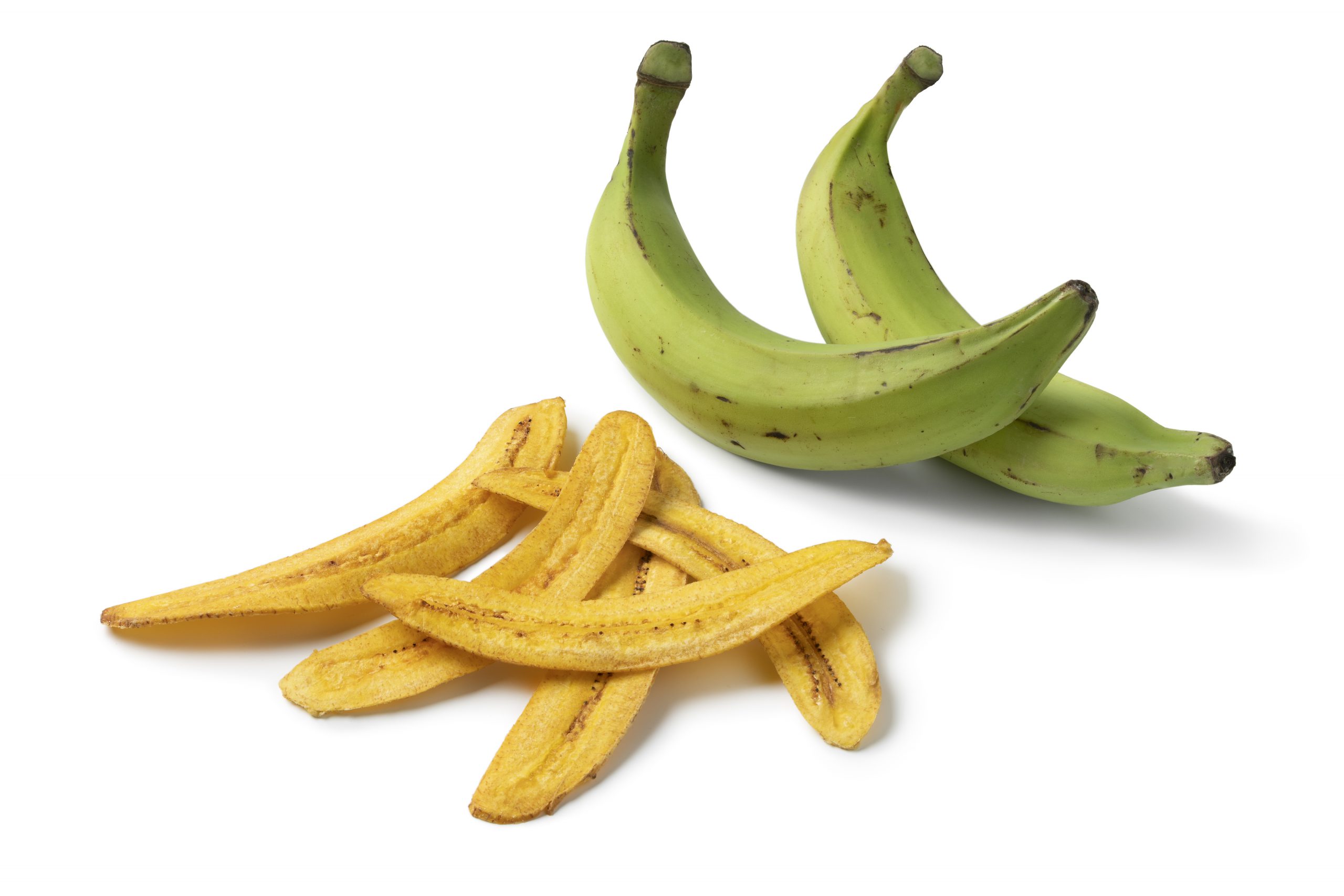 Heap of fresh baked banana chips and fresh green plantains close up isolated on white background
